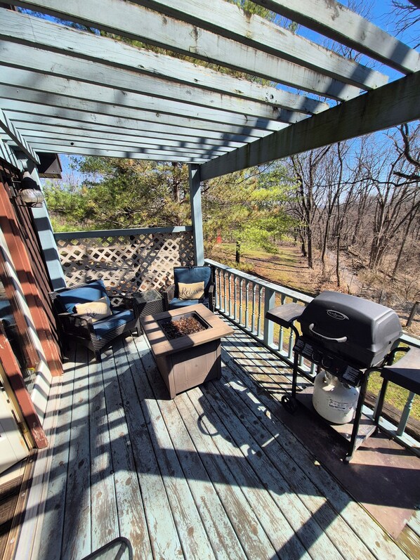 A wooden deck with a grill, outdoor seating, and a view of trees.