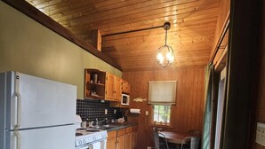 A compact kitchen with wooden cabinets, a refrigerator, stove, and a dining area with a table and chairs.