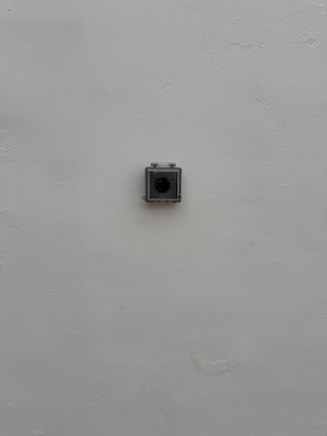 A square, metallic object mounted on a plain wall.