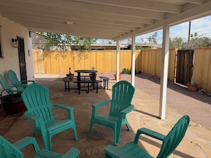 A covered patio area with outdoor seating, including chairs and a table, and a wooden fence in the background.