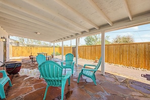 An outdoor patio with a covered area, stone flooring, and several green chairs.