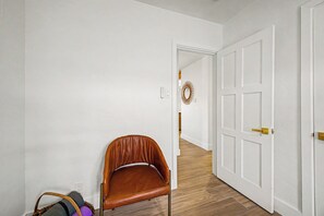 A hallway with a brown leather chair, a white door, and a wooden floor. - Charming 3-bedroom house with AC in sunny Phoenix (Phoenix)