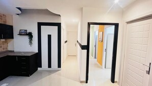 A hallway with a kitchen area on the left, a white door with black trim, and a door leading to a room with a green wall. - Urban Oasis Partition Room in Al Barsha1 (Dubai)