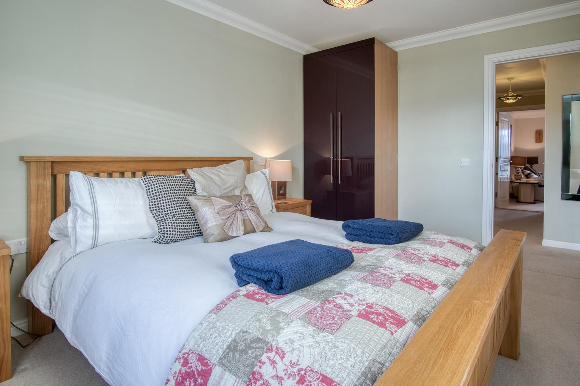 A neatly made bed with a floral quilt, a wooden headboard, and a bedside table with a lamp.