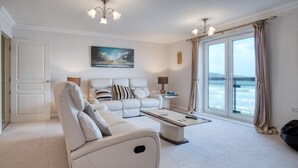 A spacious living room with a white sofa, a coffee table, and a large window with a view of the sea. - 13 St Bride's Bay View - 4 Bedroom - Broad Haven (Haverfordwest)
