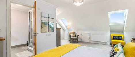 Ein Schlafzimmer mit Bett, Stuhl, gelbem Ohrensessel, Dachfenster und Heizkörper.