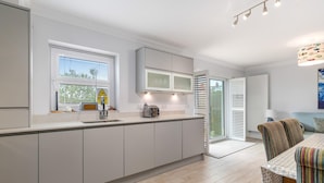 Eine moderne Küche mit weißen Schränken, einem Einbauofen und einem Fenster mit Jalousien.