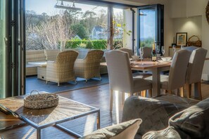 A dining area with wicker furniture, a table with a woven basket, and a view of the garden through glass doors.