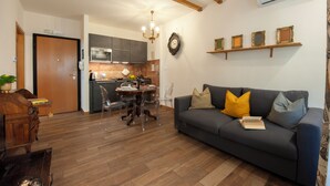 A living room with a dark sofa, wooden coffee table, and a dining area with a wooden table and chairs. A kitchen with modern appliances is visible in the background. - Casa Sorelle Flo - Flo Apartments (Florence)