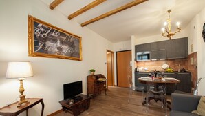 A living room with a television, wooden furniture, a dining table with chairs, and a kitchen area with cabinets and a microwave. - Casa Sorelle Flo - Flo Apartments (Florence)