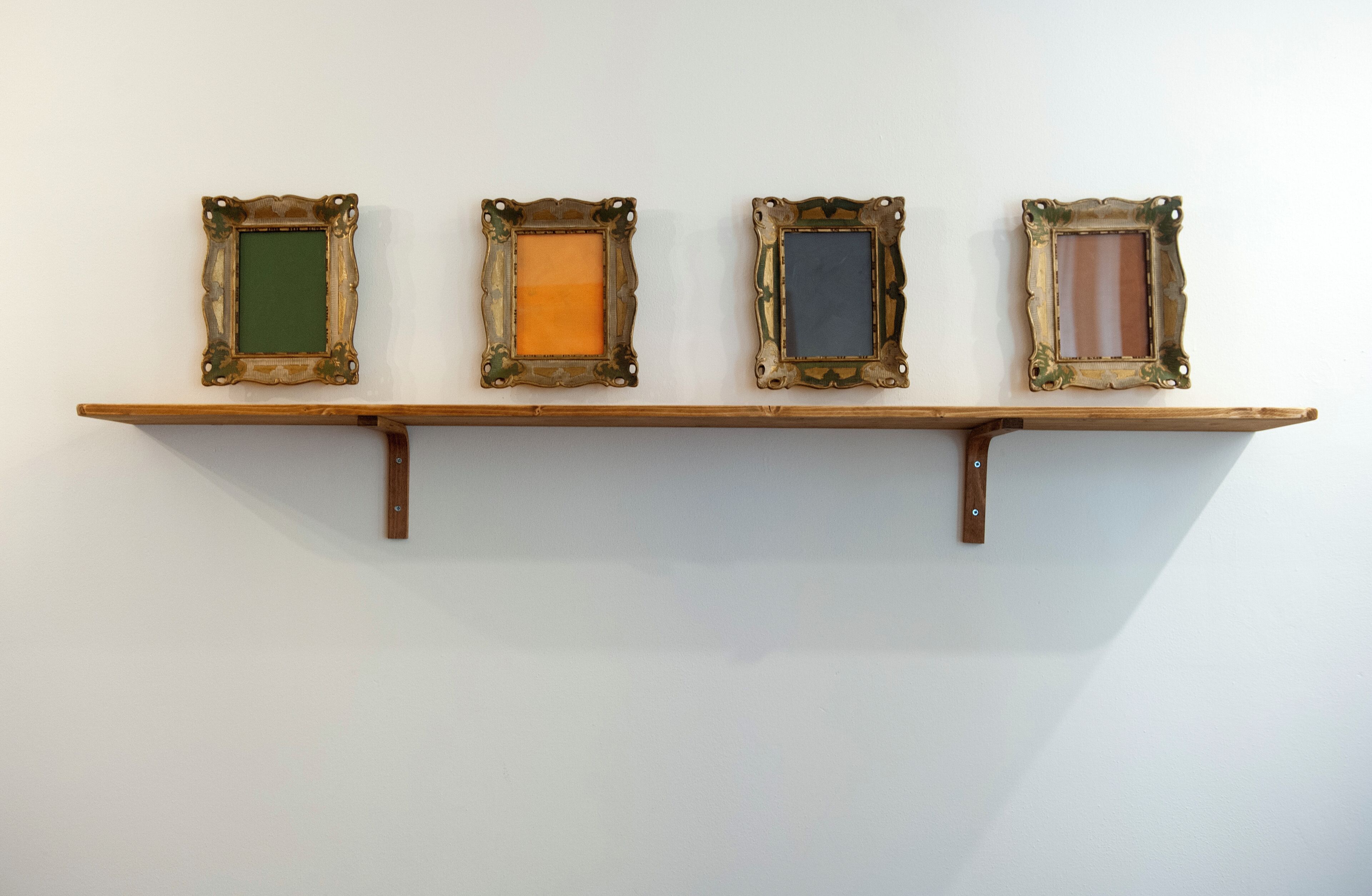 A wooden shelf with four picture frames of varying sizes and colors.