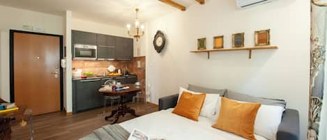 A bedroom with a bed, a bedside table, and a view of a kitchen.