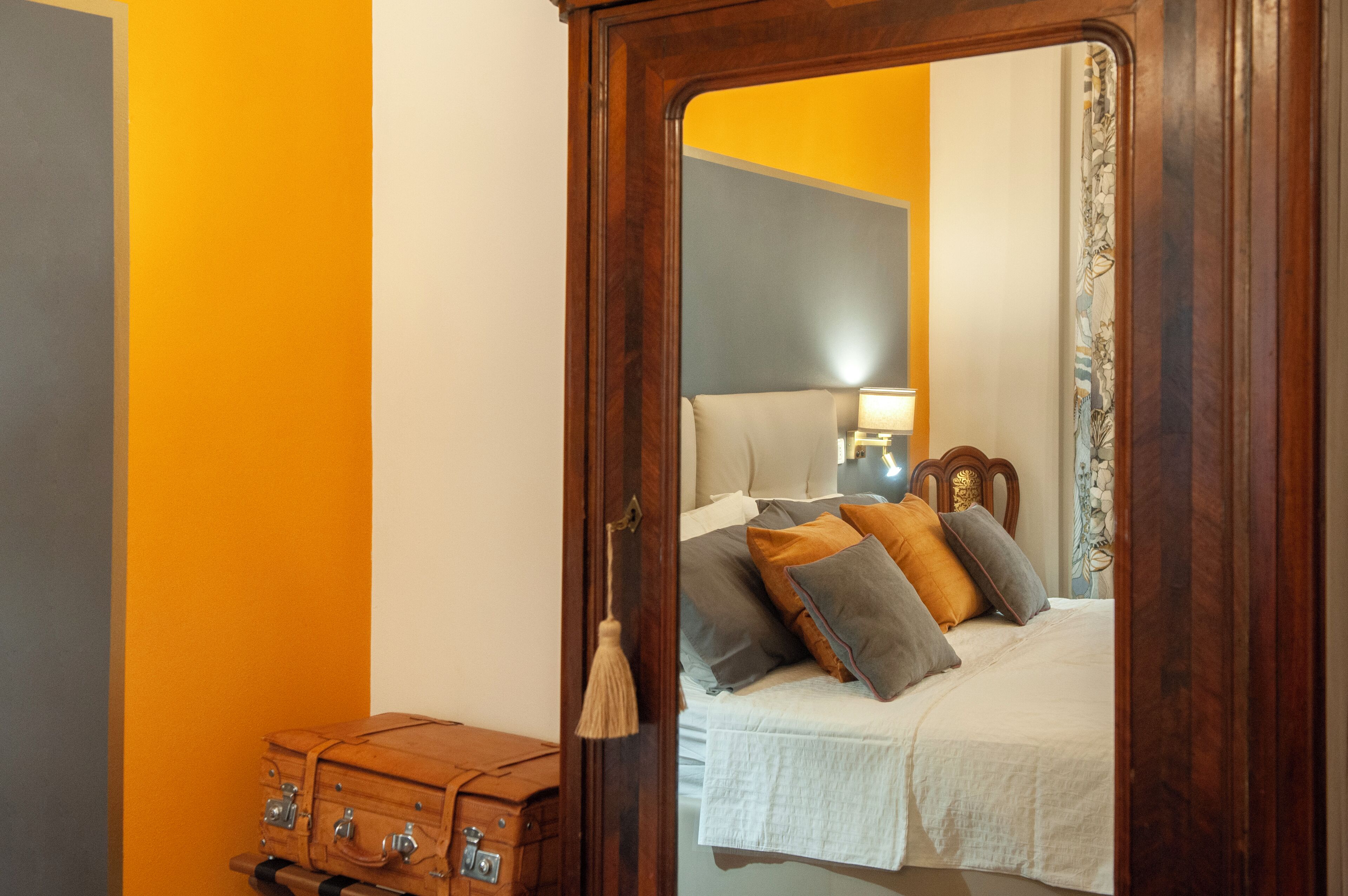 A bedroom with a bed, a wooden dresser, and a mirror reflecting the room.