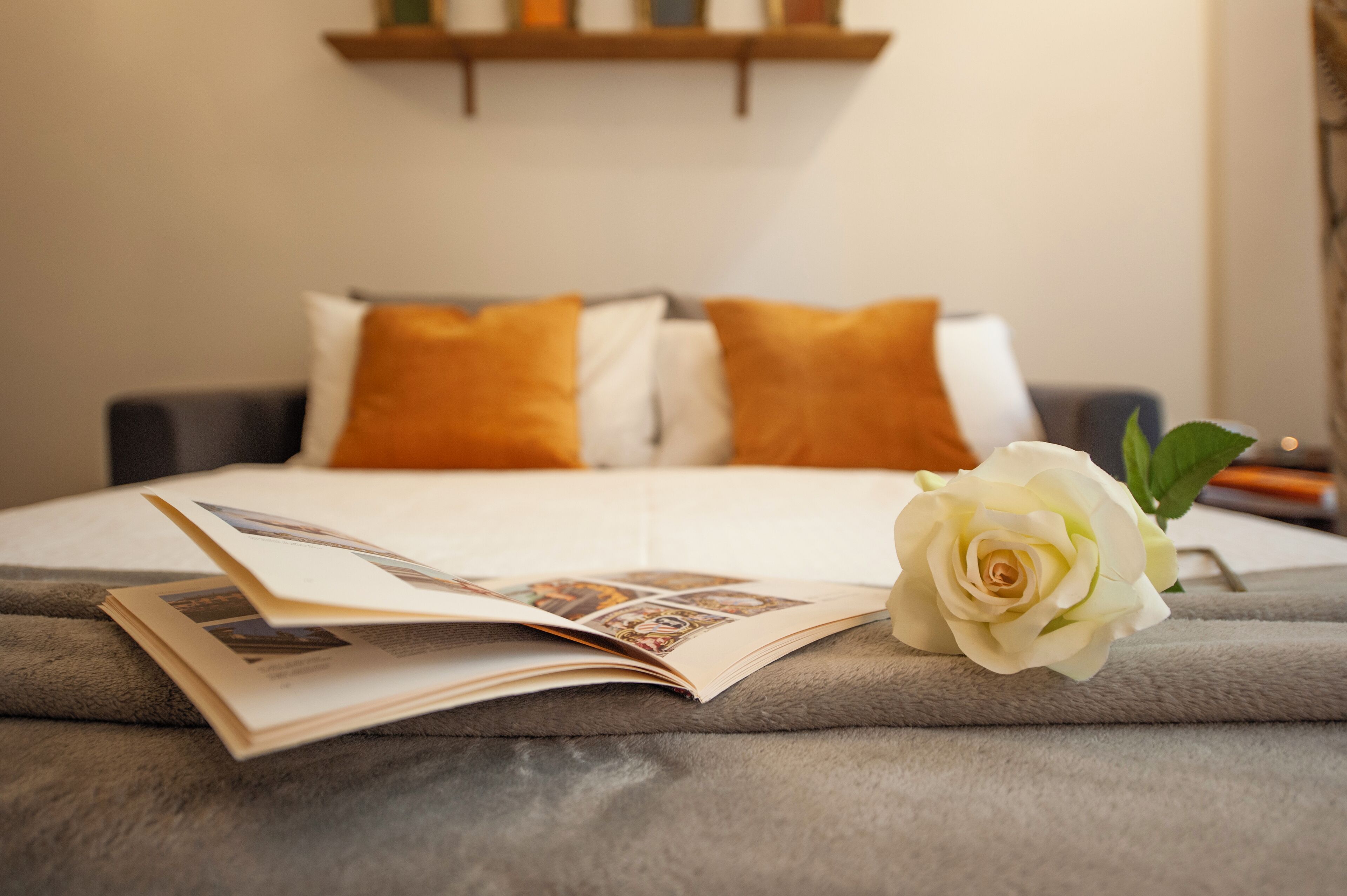 A neatly made bed with a book and a white rose on the bedspread.