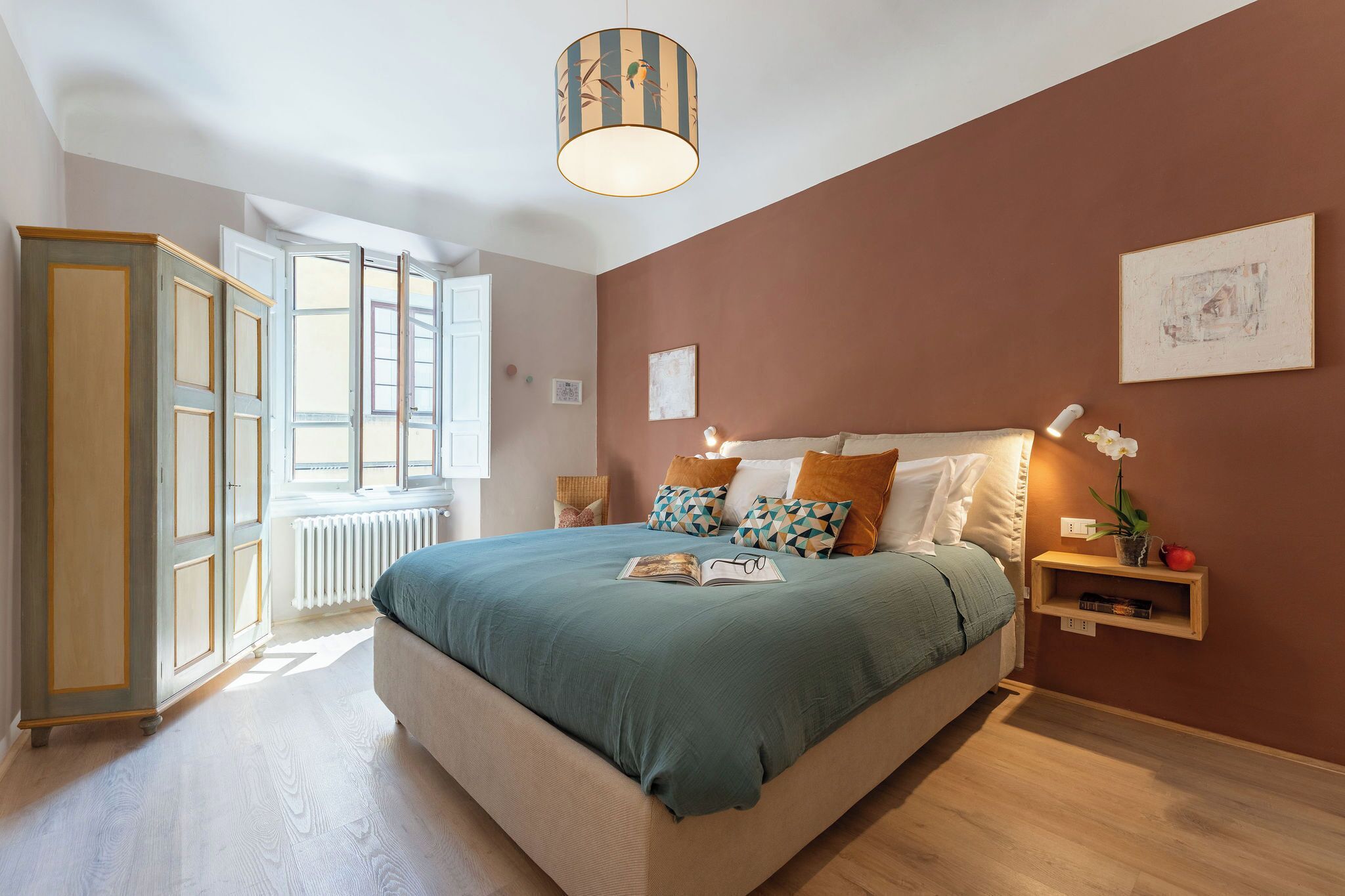 A bedroom with a large bed, a bedside table with a lamp, a window, and a wardrobe.