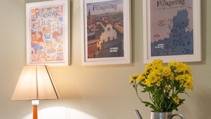 Un escritorio con una lámpara, un florero con flores amarillas y tres carteles enmarcados en la pared.