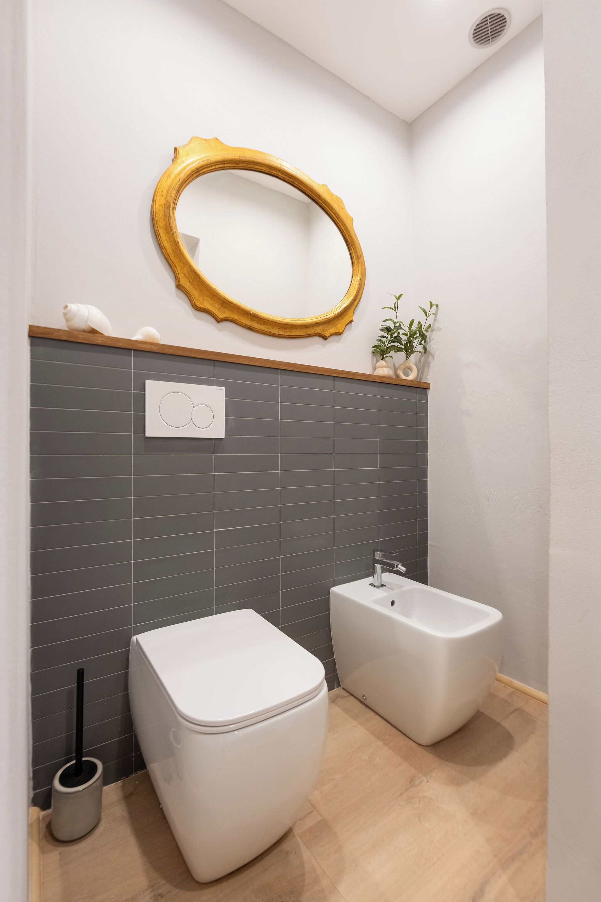 A modern bathroom with a toilet, bidet, and a large mirror with a gold frame.
