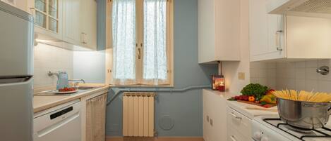 A compact kitchen with white cabinets, a stove, and a window with curtains.