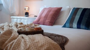 A neatly made bed with a striped pillow, a bedside lamp, and a basket with a cup and a book. - Ricasoli 37 - Flo Apartments (Florence)