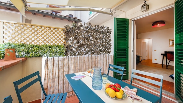 A dining area with a table set for two, a basket of fruit, and a pitcher of water. - Ricasoli 37 - Flo Apartments (Florence)
