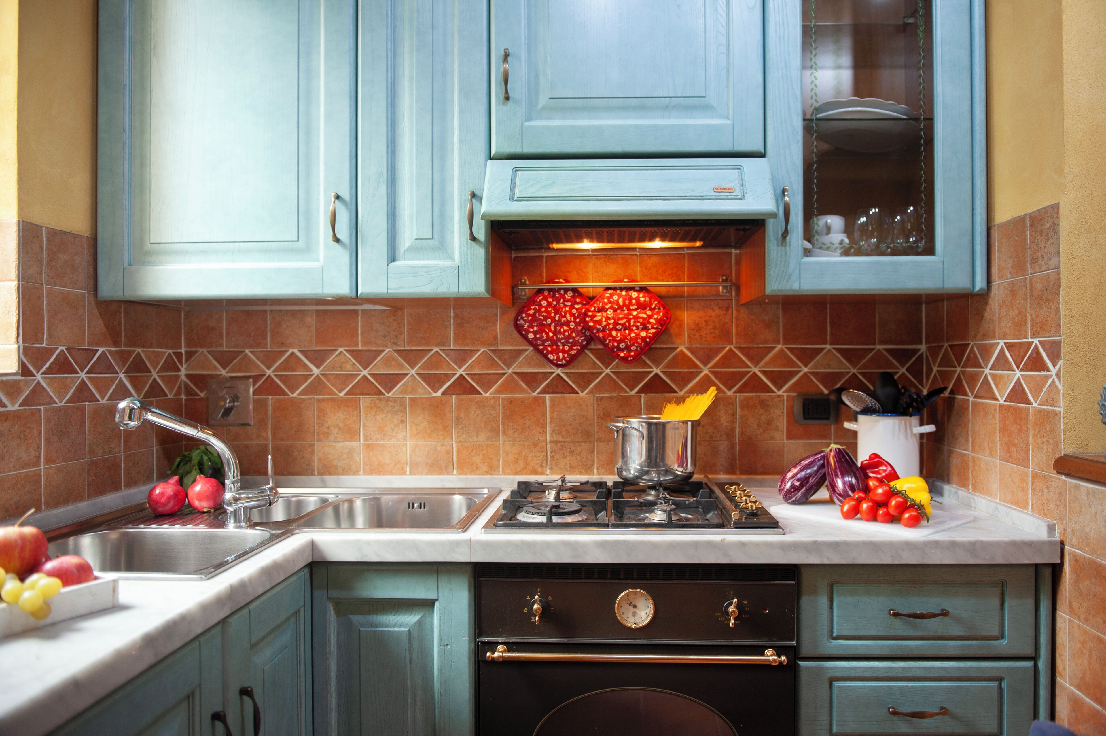 A kitchen with teal cabinets, a gas stove, a sink, and a tiled backsplash.