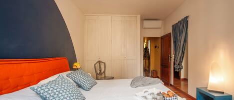 Un dormitorio con cama, almohadas, mesita de noche con lámpara, bandeja con alimentos para el desayuno y armario.