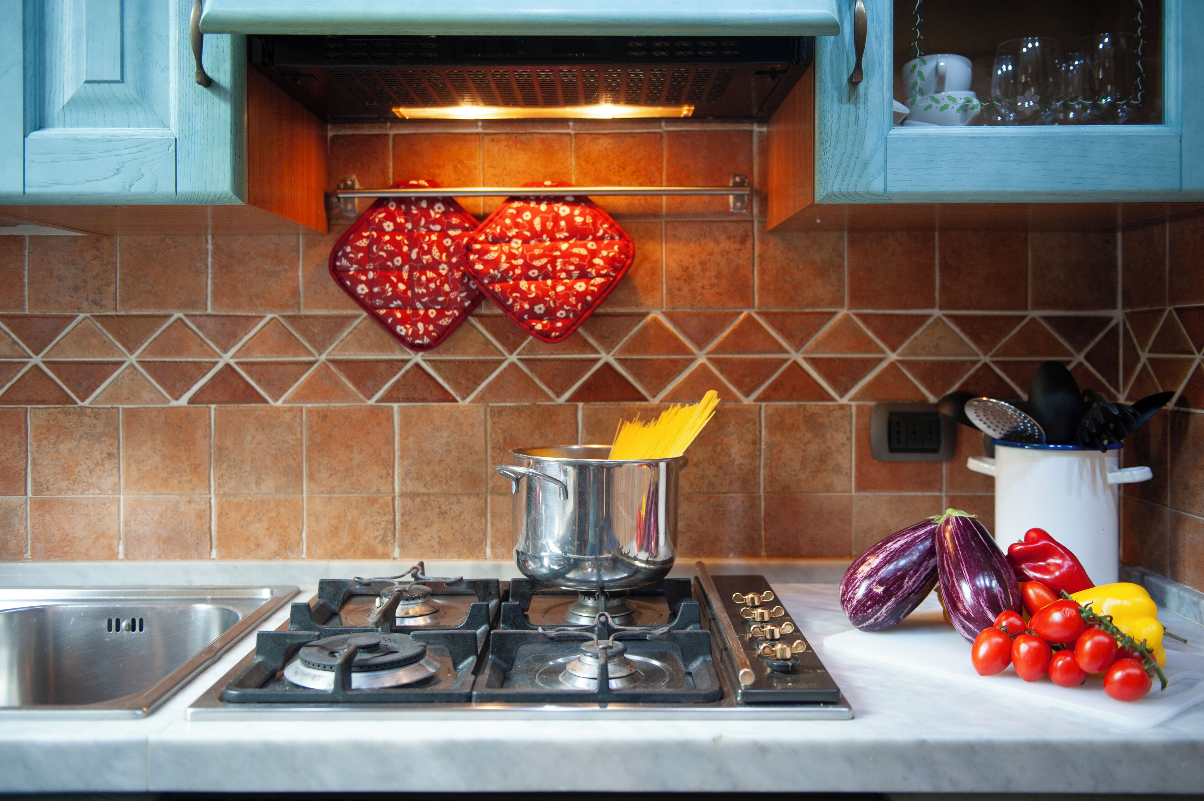 Una cocina con estufa a gas, una olla en la hornilla y varios vegetales sobre la encimera.