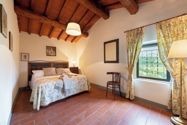A bedroom with a bed, a chair, a window with curtains, a lamp, and a picture on the wall. - La Casa di Madina - Flo Apartments (Montespertoli)