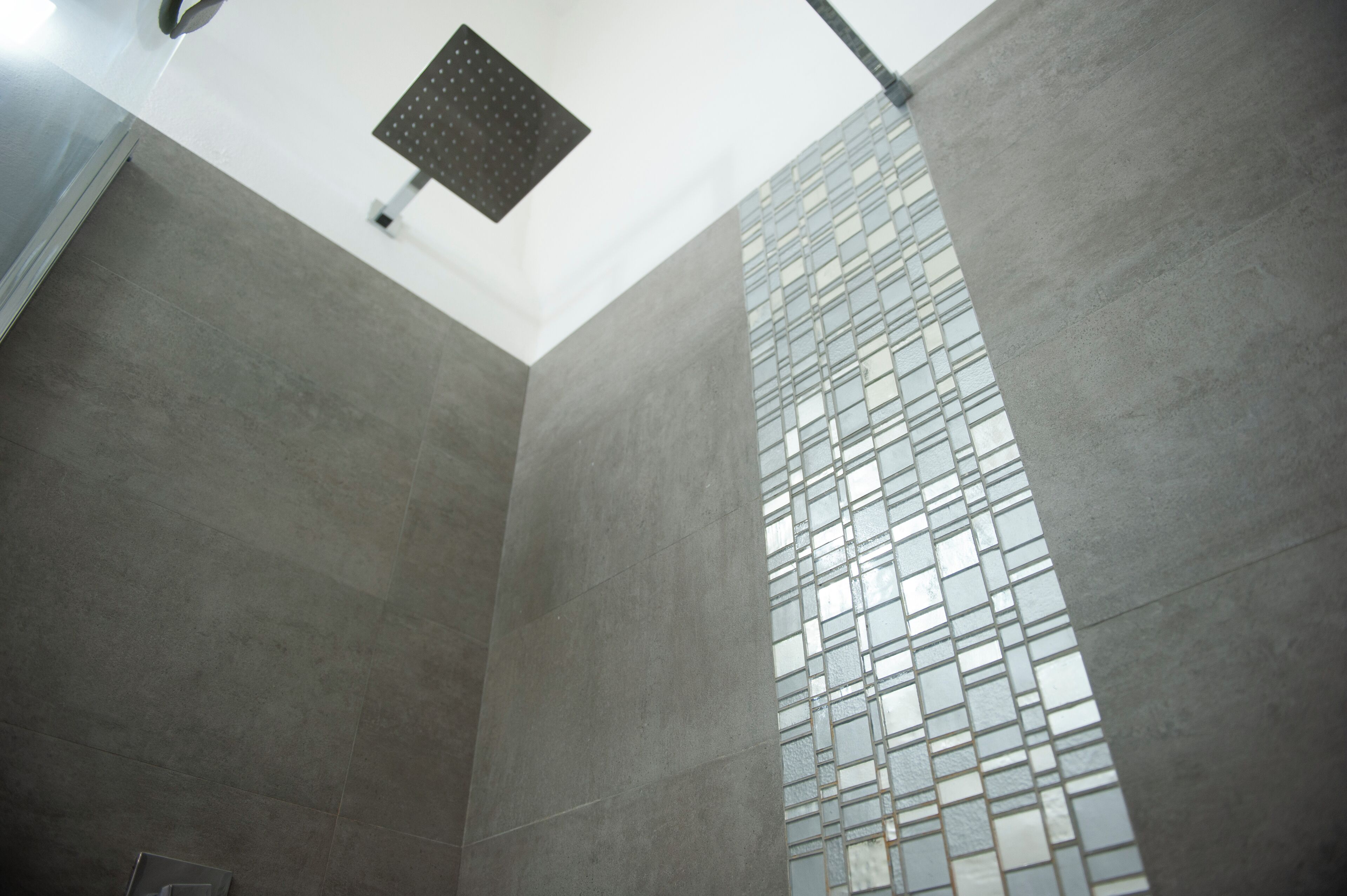 A modern bathroom with a large tiled wall and a ceiling-mounted shower.
