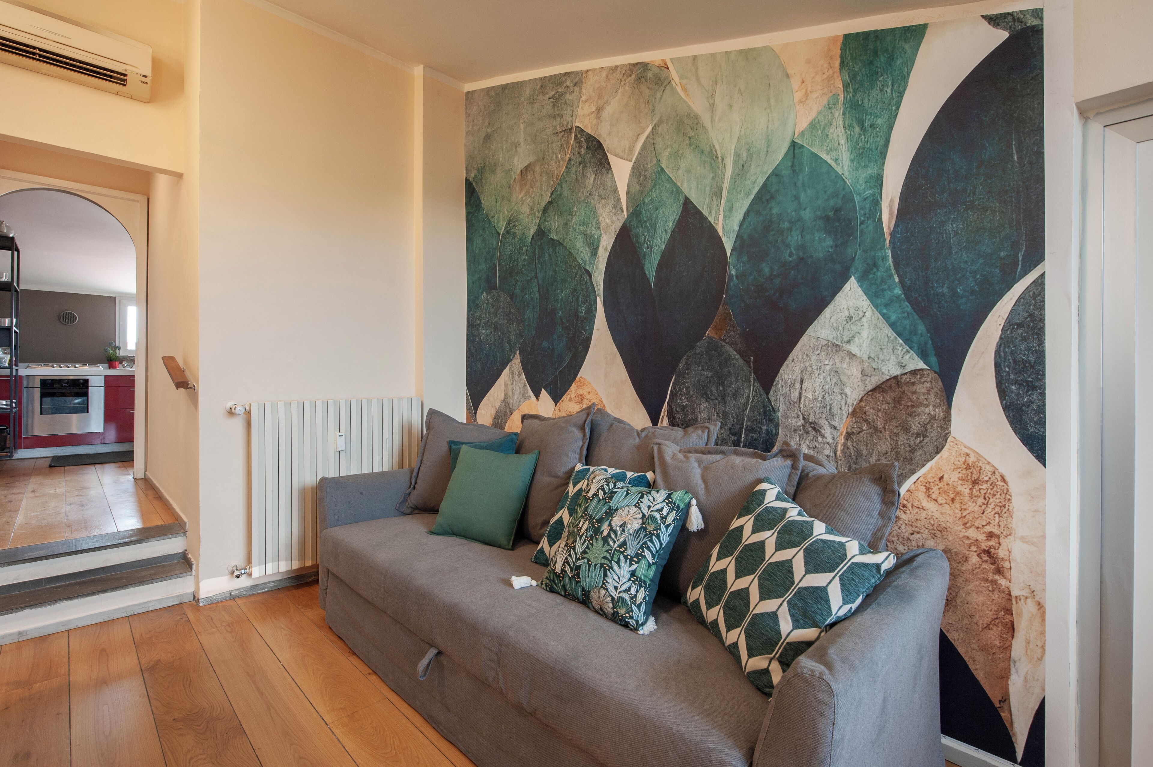Een woonkamer met een bank, kussens en een muur met een geometrisch patroon.