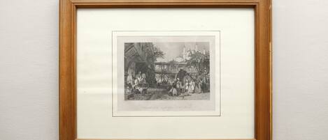 A framed black and white historical illustration of a bustling market scene with buildings and people.
