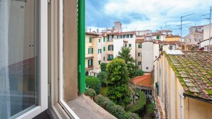 Blick aus einem Fenster auf eine schmale Straße mit traditionellen Gebäuden, einen kleinen Garten und einen klaren Himmel.