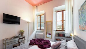 A bedroom with a bed, a desk, a TV, a window with curtains, a mirror, and a bookshelf. - Pitti - Flo Apartments, Charme su Piazza Pitti (Florence)