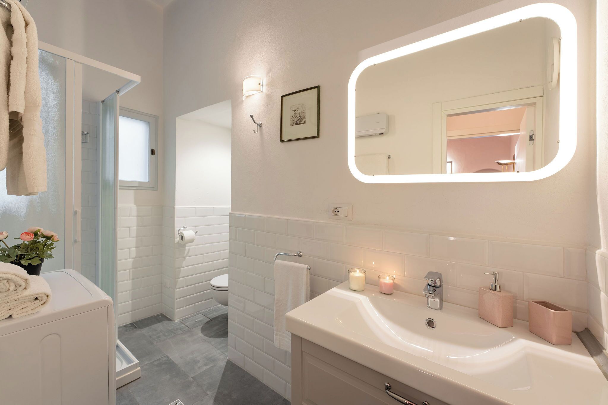A bathroom with a white sink, mirror, and towel rack. There is a shower area with a glass door and a window.