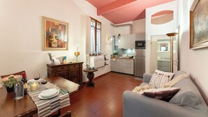 A living room with a dining table set, a sofa, a kitchen in the background, and a painting on the wall. - Pitti - Flo Apartments, Charme su Piazza Pitti (Florence)