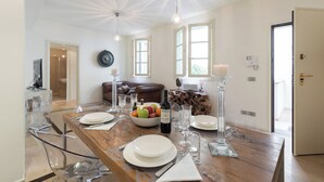A dining area with a wooden table set for four, a bowl of fruit, and a bottle of wine. - Boboli - Flo Apartments (Florence)