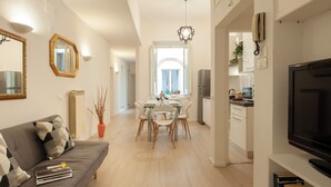 Un salon moderne avec un canapé, une table à manger et des chaises. On aperçoit un téléviseur sur la droite et, au fond, un coin cuisine.
