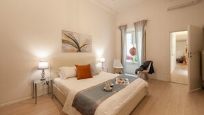 Une chambre d’hôtel moderne avec un grand lit, des lampes de chevet, une petite table sur laquelle se trouve un plateau avec divers objets, et une vue sur l’extérieur par une fenêtre.