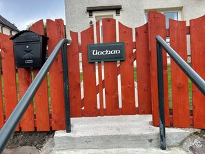A red wooden gate with a sign reading "Uochan" and a black mailbox on the left. - Welcome to Your Highland Escape in Corpach (Fort William)