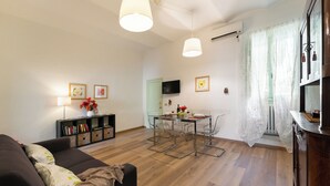 A modern living room with a sofa, a glass dining table, and a TV mounted on the wall. - Campuccio - Flo Apartments (Florence)