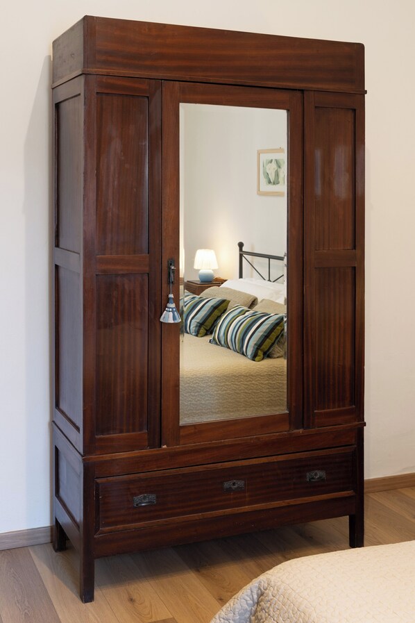 A wooden wardrobe with a mirror, drawers, and a bed with pillows in the background. - Campuccio - Flo Apartments (Florence)