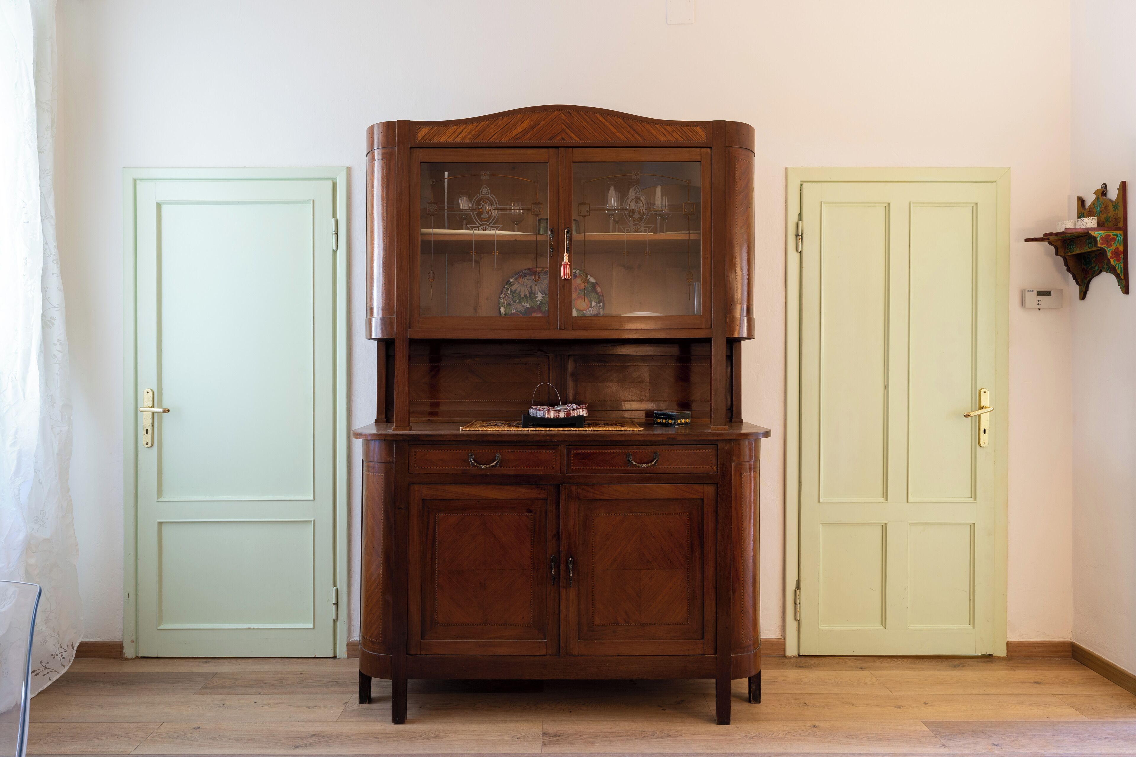 A wooden cabinet with glass doors, positioned between two doors.