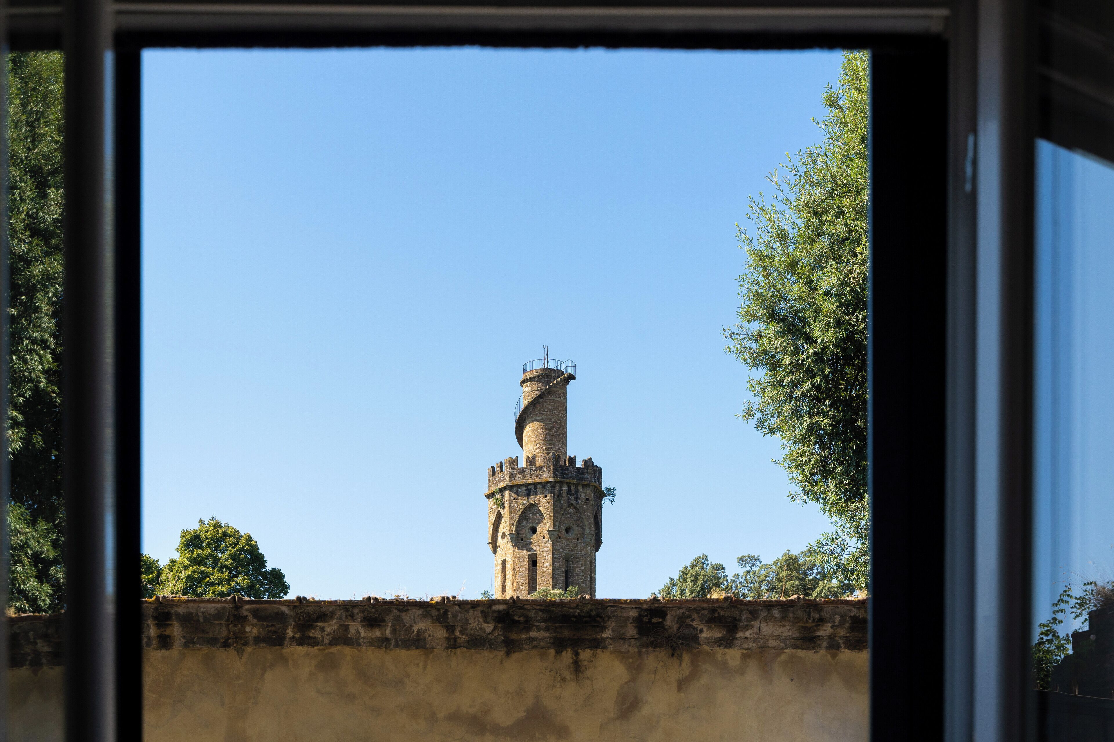 Ein historischer Turm mit einer Wendeltreppe, umgeben von Bäumen und blauem Himmel.