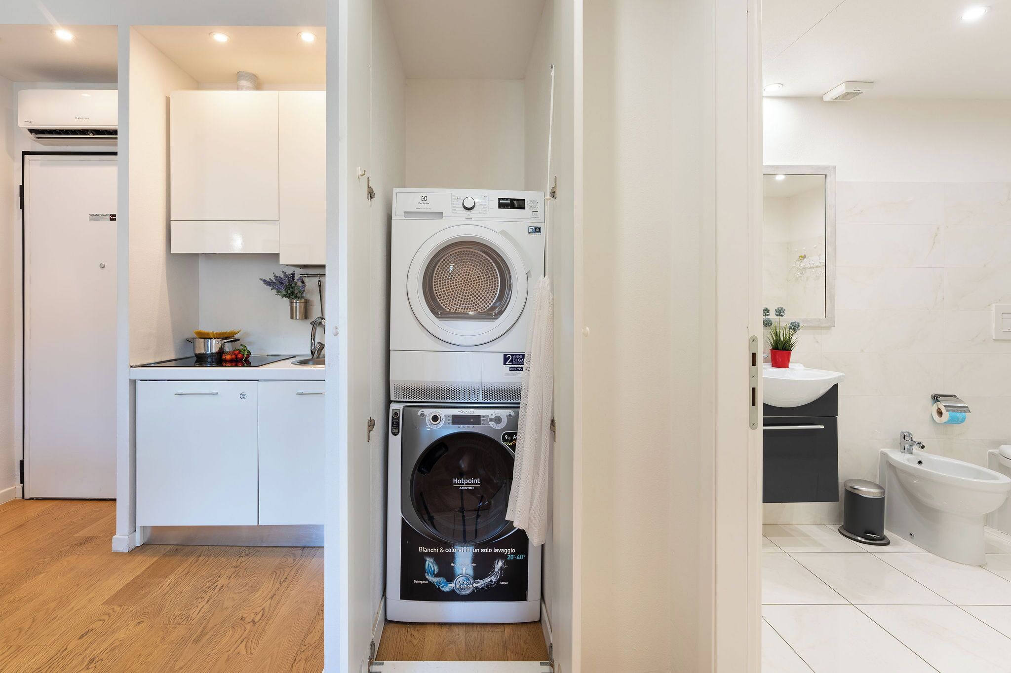 A compact laundry room with a front-loading washing machine and dryer, adjacent to a kitchen area with white cabinets and a sink.