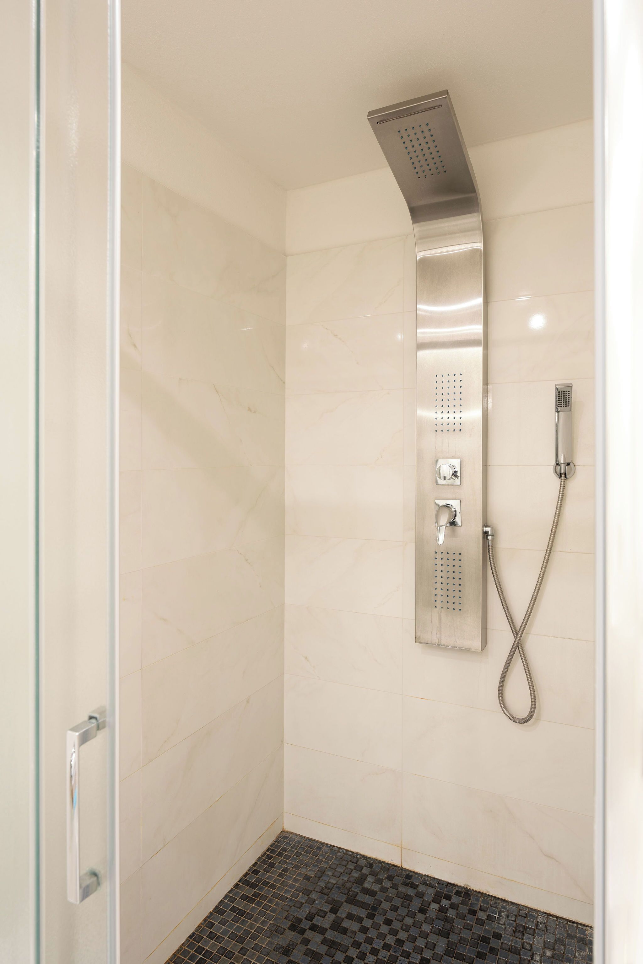 Una ducha con cabezal de ducha manual y cabezal de pared fijo, ambos con mandos.