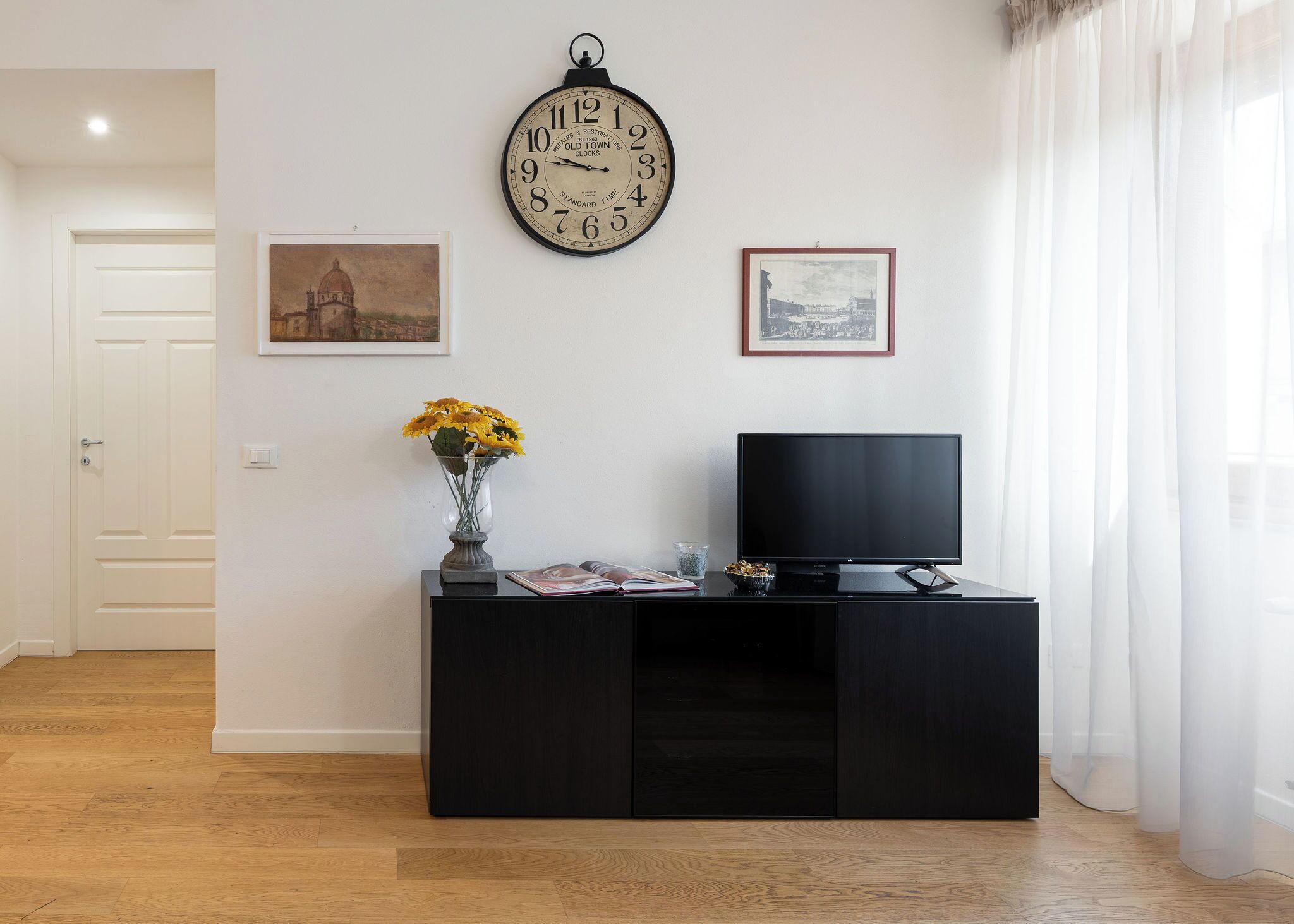 A modern living room with a black entertainment unit, a wall clock, and two framed pictures.