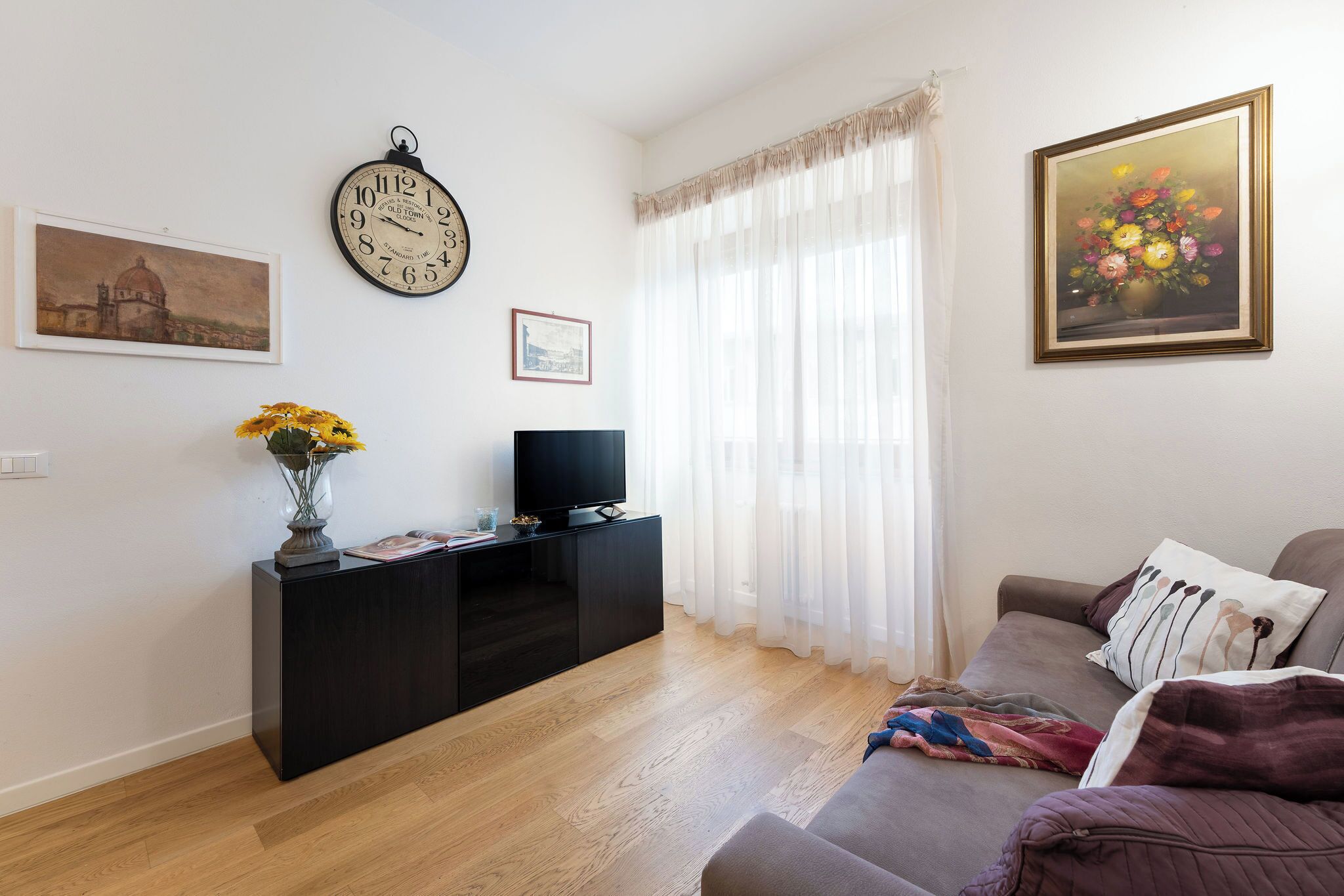 Ein Wohnzimmer mit einer schwarzen Unterhaltungsanlage, einer Couch, einem Fernseher und einem Blumenbild.