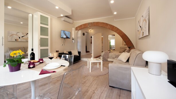 A modern living room with a dining area, featuring a white sofa, a grey sofa, a white coffee table, and a dining table with clear chairs. - Fossi - Flo Apartments (Florence)