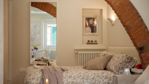 A bedroom with a bed, a mirror, a radiator, and a brick archway. - Fossi - Flo Apartments (Florence)