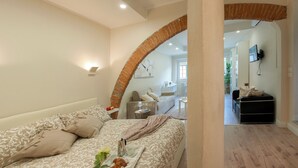 A modern bedroom with a large bed, a sitting area with a sofa and a coffee table, and a view into the living room. - Fossi - Flo Apartments (Florence)